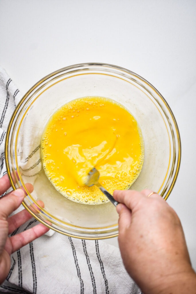 Hands whisking eggs together in a bowl.