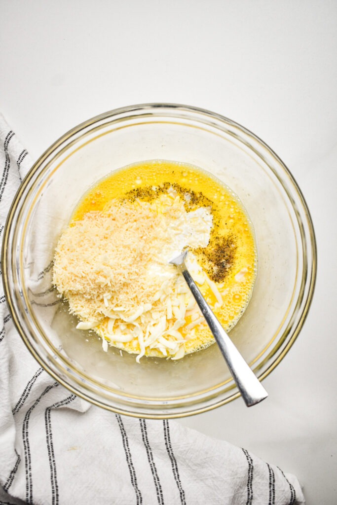 Cheeses and seasonings added to the eggs in a bowl.