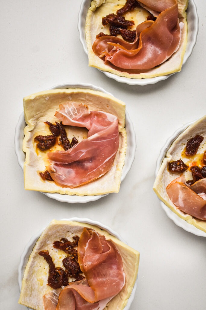 Prosciutto and sun dried tomatoes placed on top of the puff pastry squares.