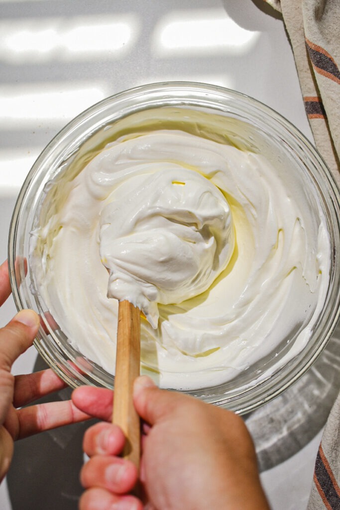 Folding condensed milk into the freshly whipped cream.