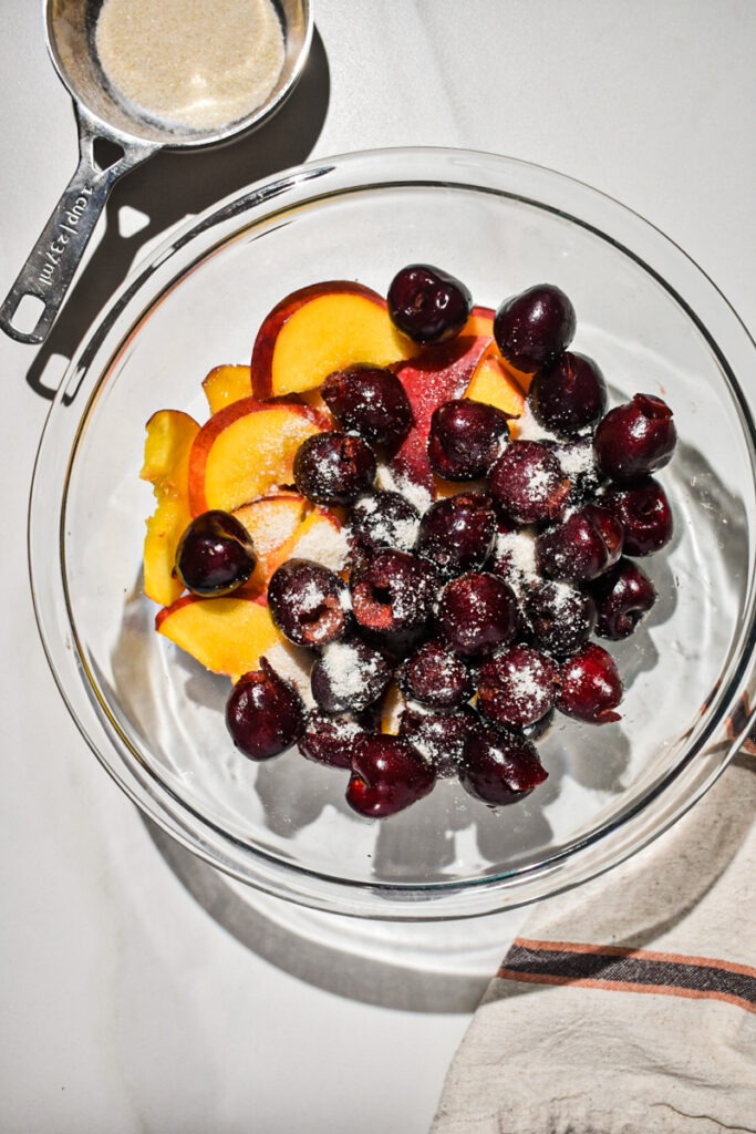 Coating the peaches and cherries in sugar in a bowl.
