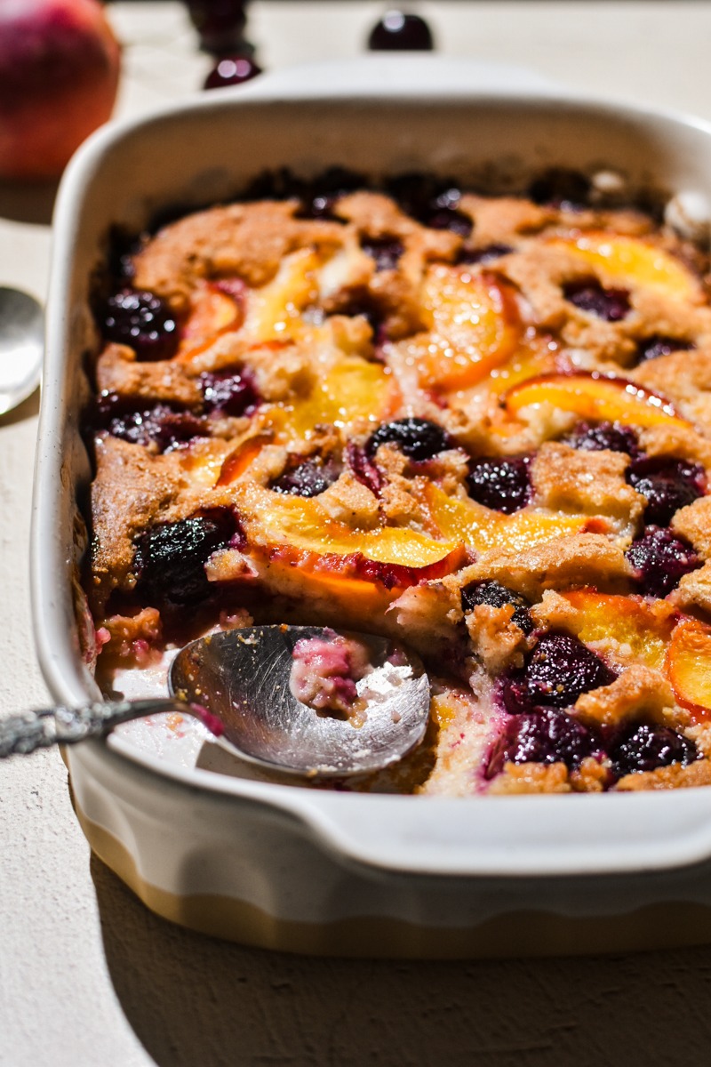 Side view of old-fashioned peach cobbler in a white baking dish with a portion missing.