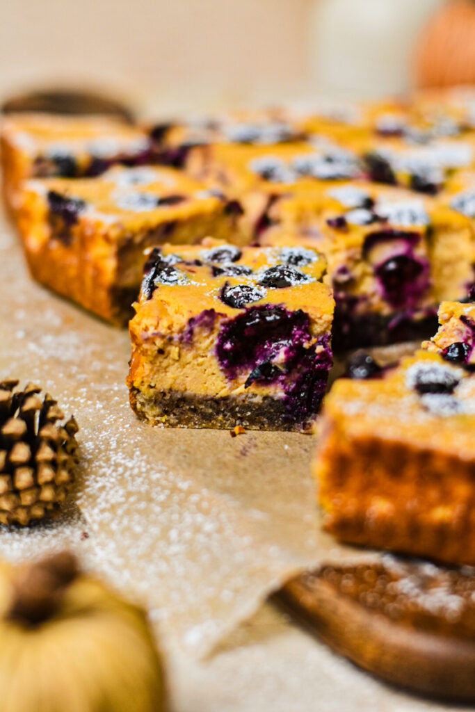 Close-up of a sliced pumpkin blueberry cheesecake bar dusted with powdered sugar.