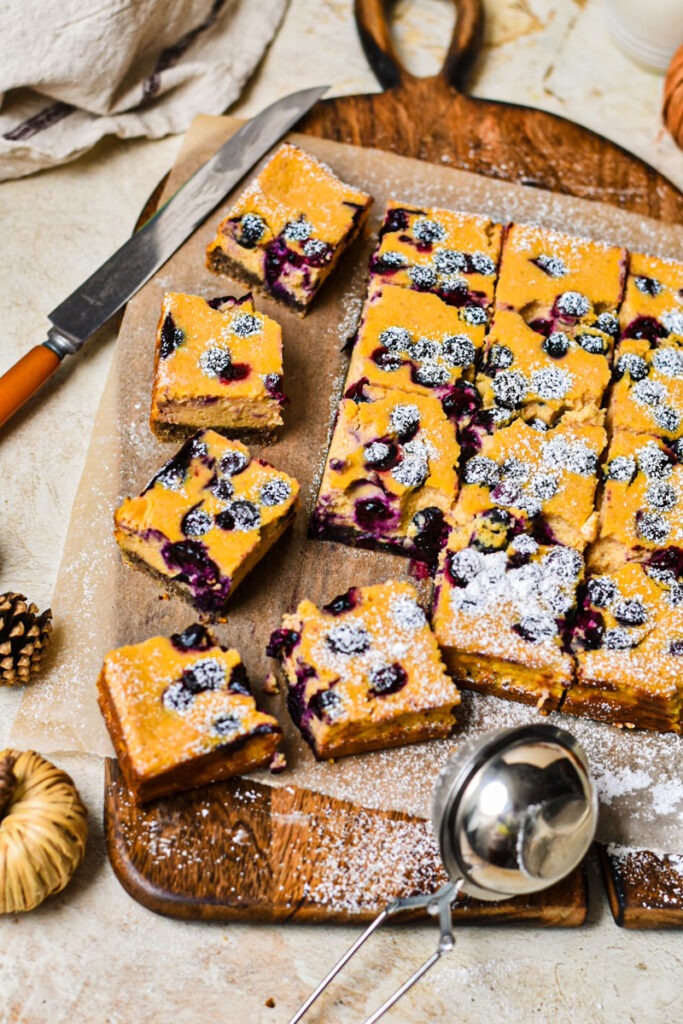 Pumpkin blueberry cheesecake bars cut into squares with powdered sugar on top