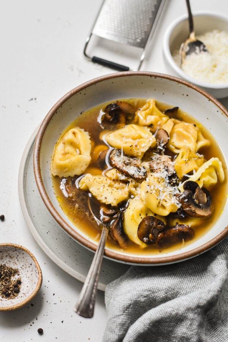 Tortellini in brodo with mushrooms served in a speckled bowl.