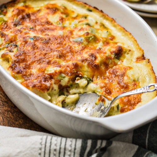 Side view of roasted cauliflower casserole with leeks and pancetta with a serving spoon.