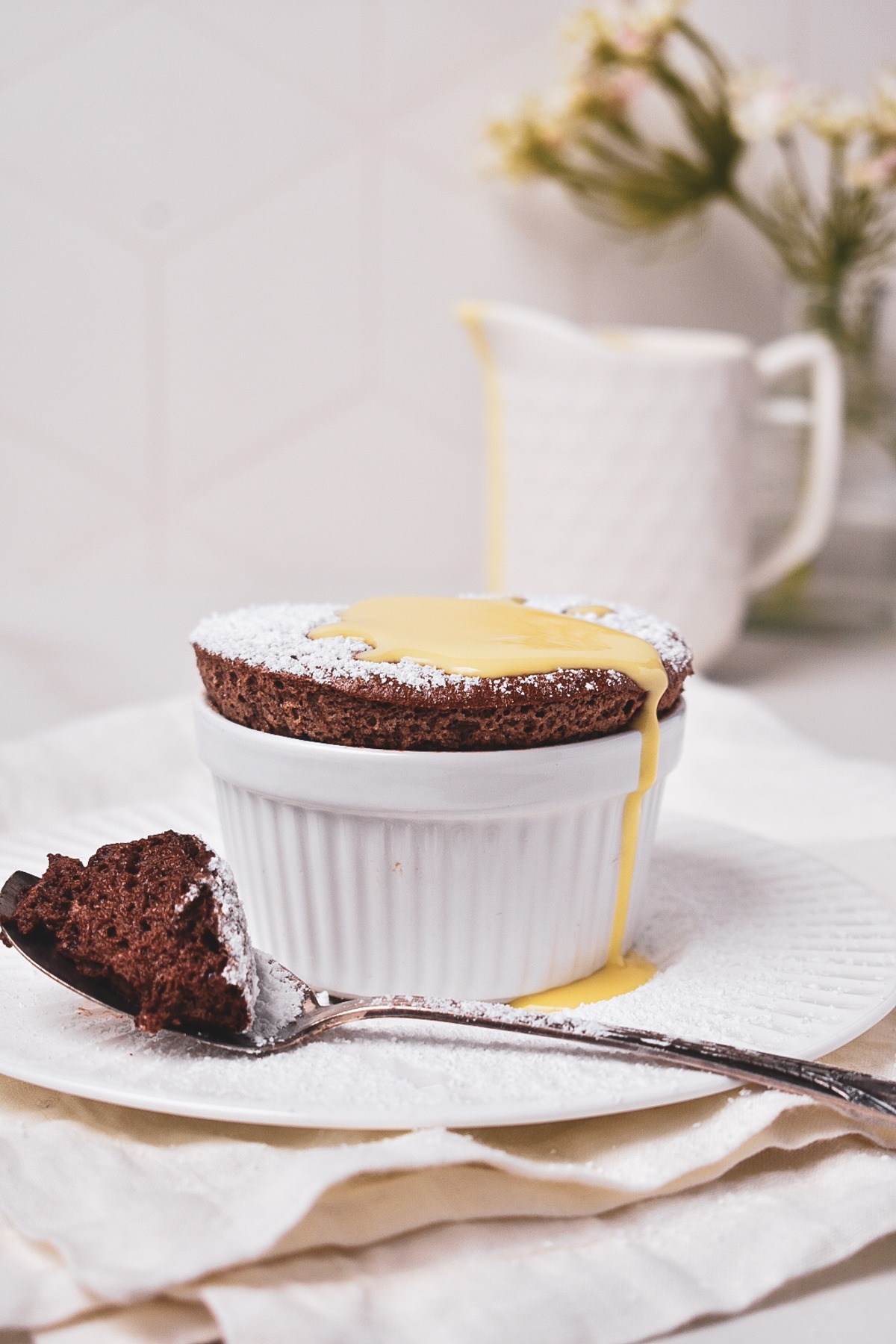 Chocolate soufflé with creme anglaise on top with a spoon with souffle on it.