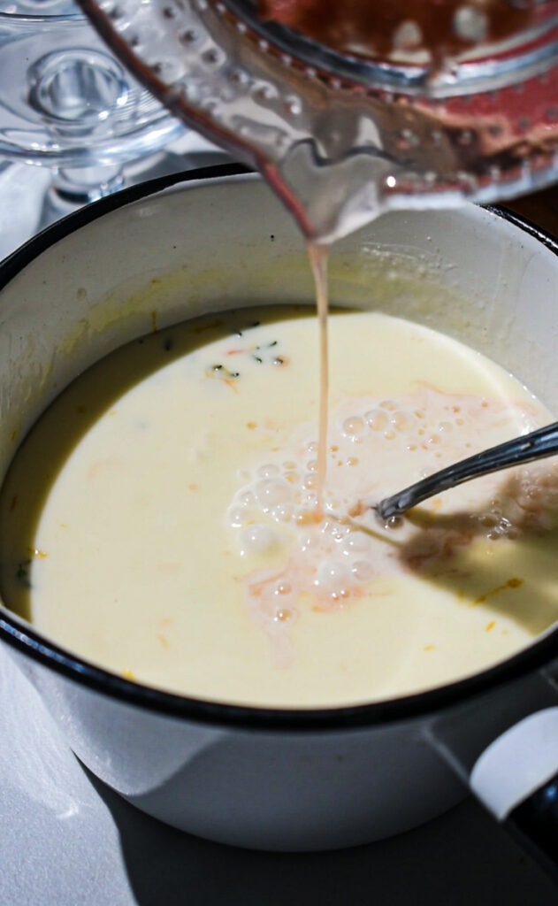 Pouring grapefruit juice into the heavy cream and thyme sprig in a saucepan.