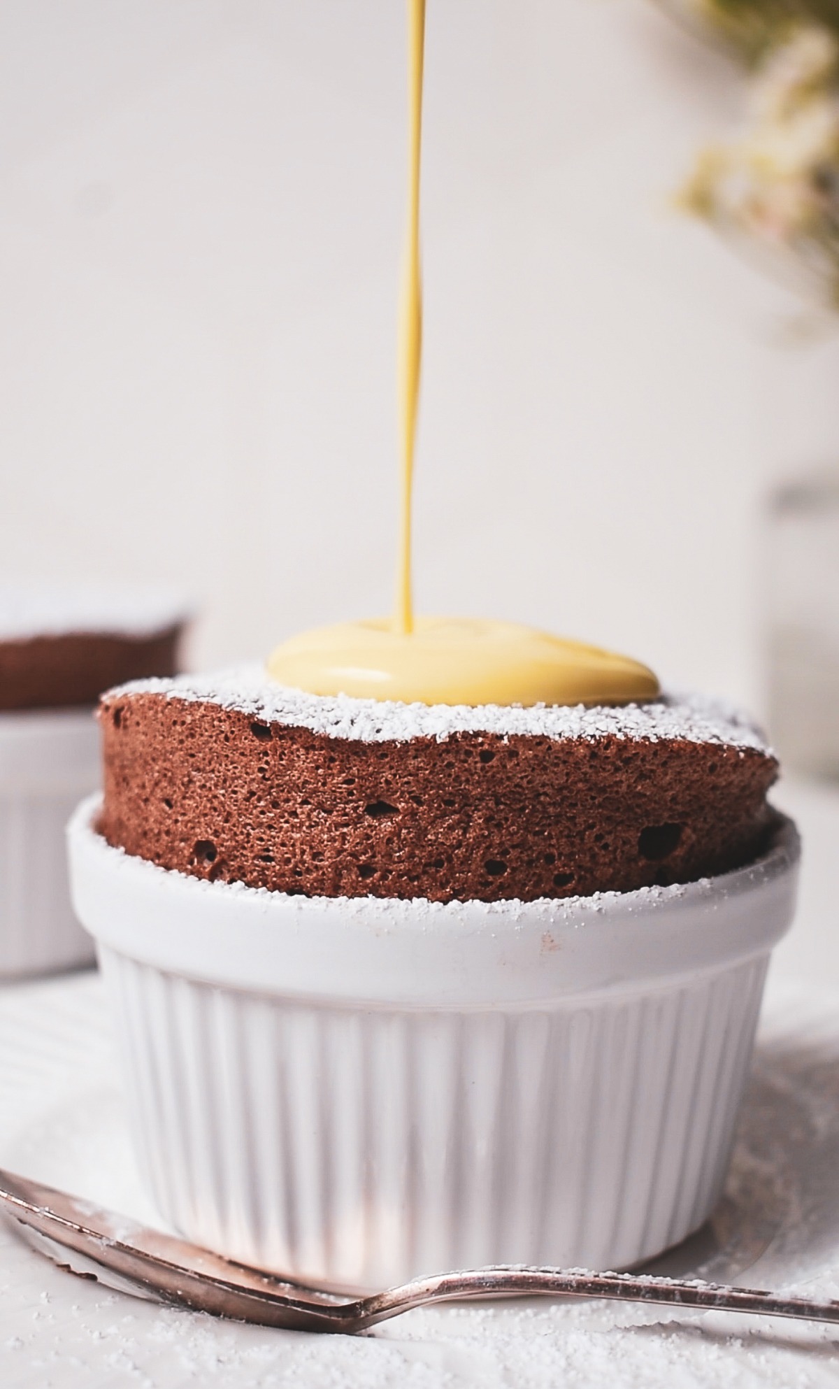 Pouring creme anglaise on top of a chocolate soufflé in a white ramekin.