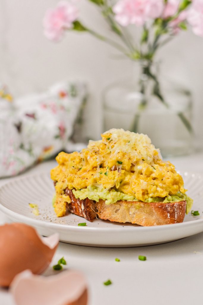 Slice of avocado toast piled high with creamy eggs with cottage cheese.