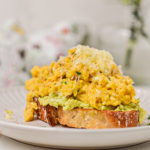 Side view of a piece of avocado toast piled high with creamy eggs with cottage cheese.