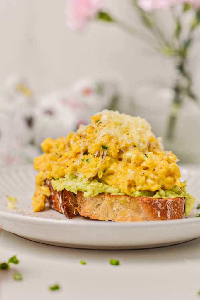 Side view of a piece of avocado toast piled high with creamy eggs with cottage cheese.