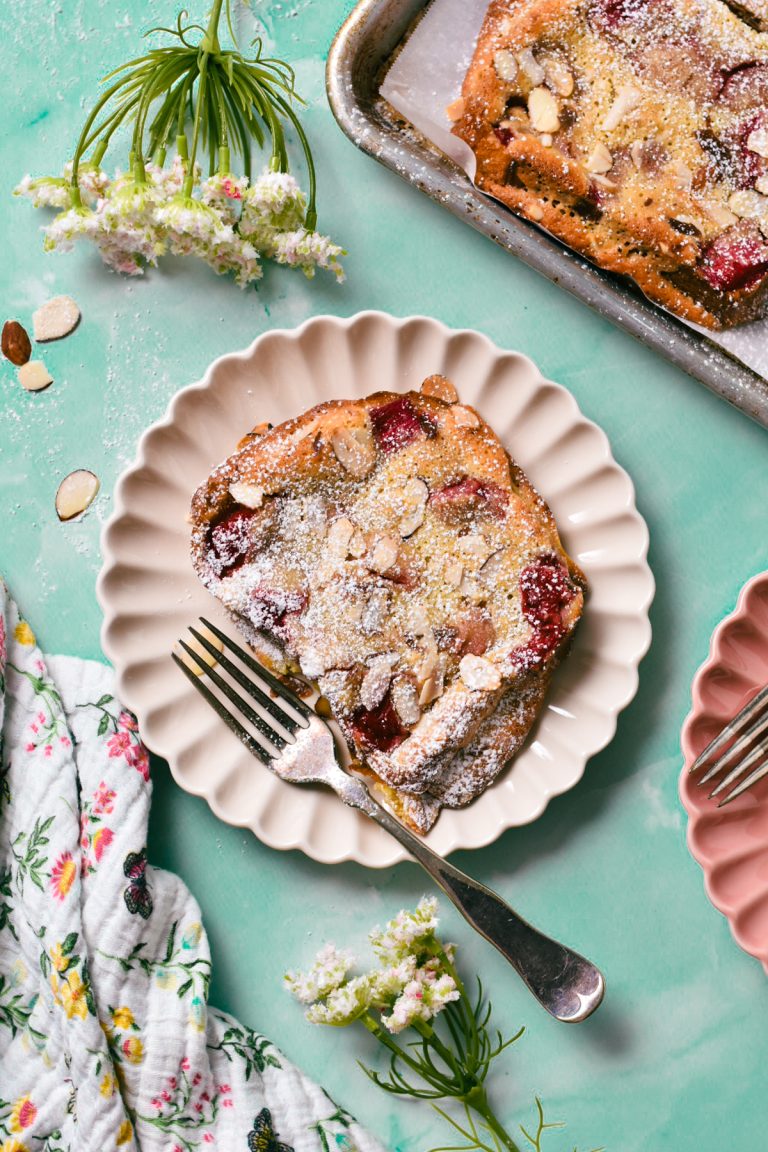 Slice of bostock with rhubarb compote on a fluted plate with powdered sugar on top.