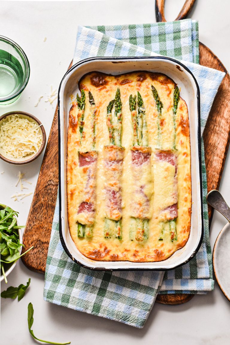 Ham and asparagus gratin with parmesan mornay sauce in a baking dish on a wooden board.