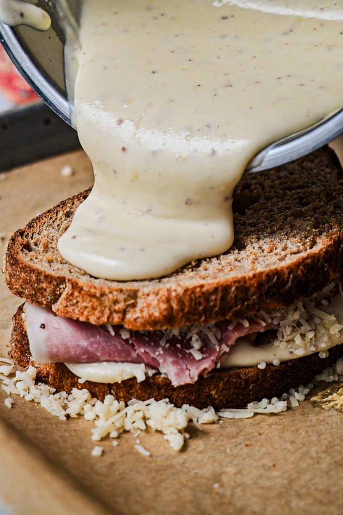 Pouring more bechamel sauce on top of the ham sandwich.