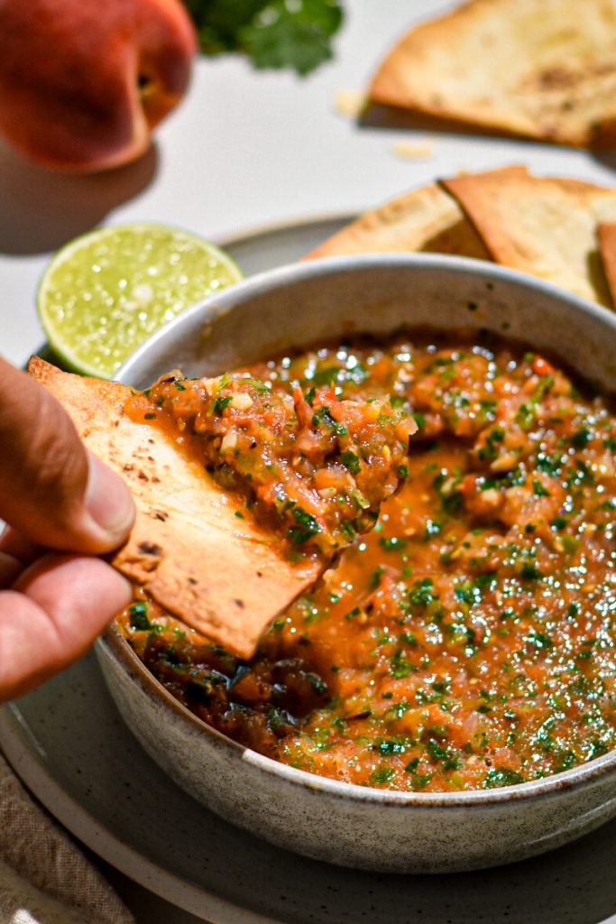 Hand dipping a tortilla chip in grilled peach and tomato salsa.