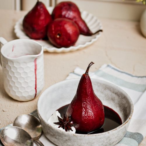 Poached pears in spicy red wine served in a bowl with a dollop of whipped cream.