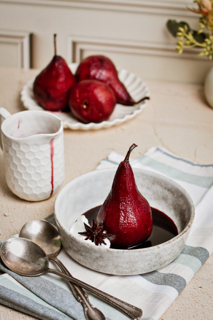 Poached pears in spicy red wine served in a bowl with a dollop of whipped cream.