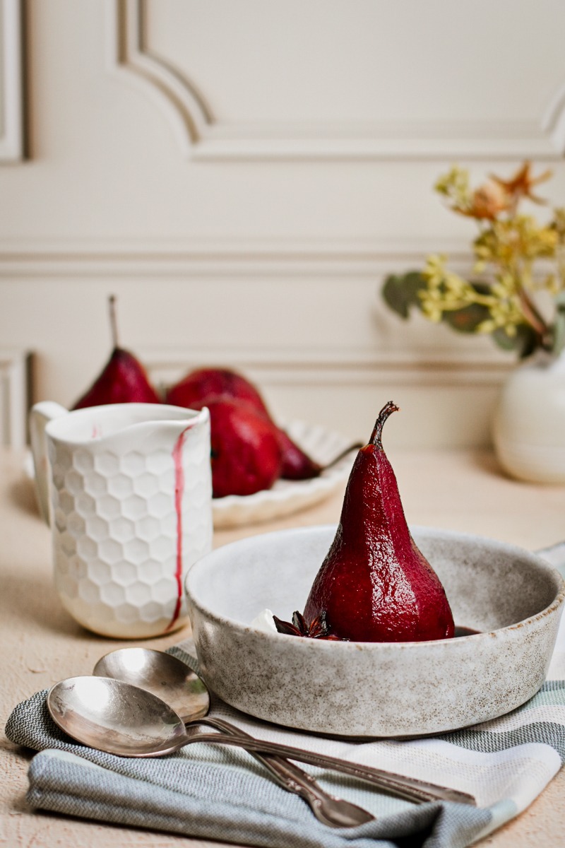 Side view of a red wine poached pear in a bowl with the stem still intact.