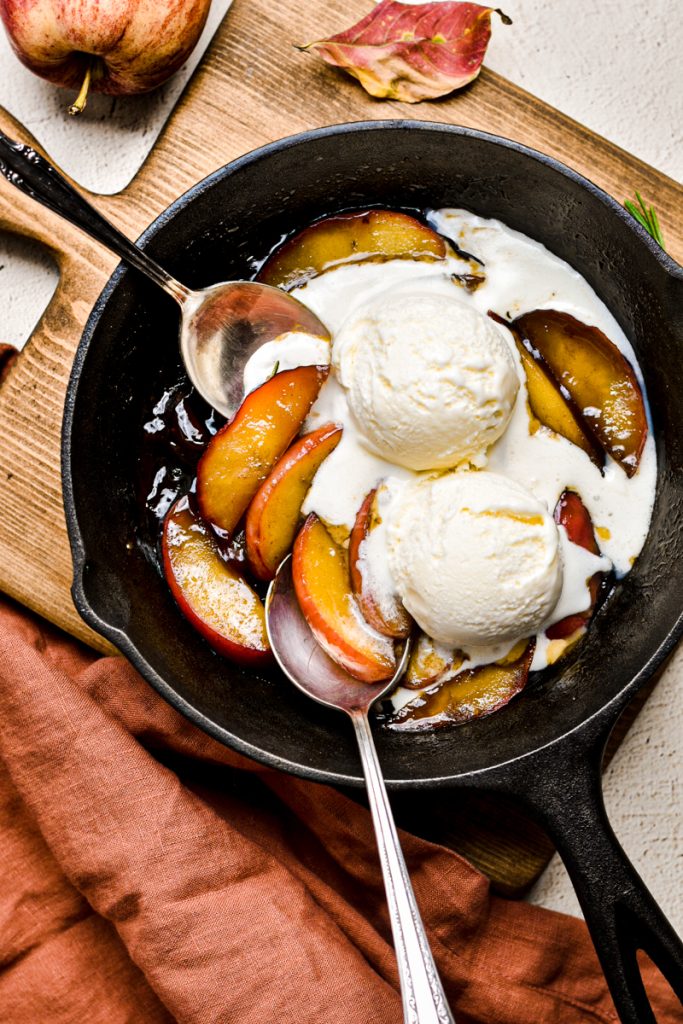 Overhead shot of apples flambé in a cast iron skillet with ice cream.