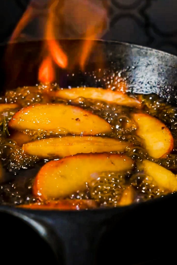 Apples flambé in a cast iron skillet with flames.