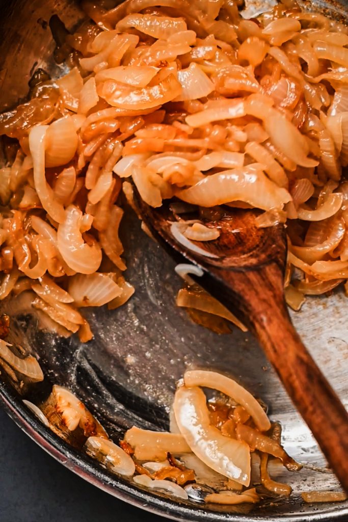 Caramelizing onions in a skillet with a wooden spoon.