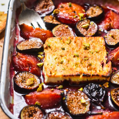 Side view of baked feta with figs and plums in a baking dish.
