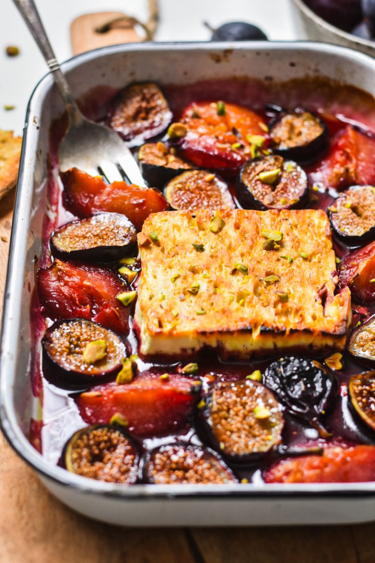 Side view of baked feta with figs and plums in a baking dish.