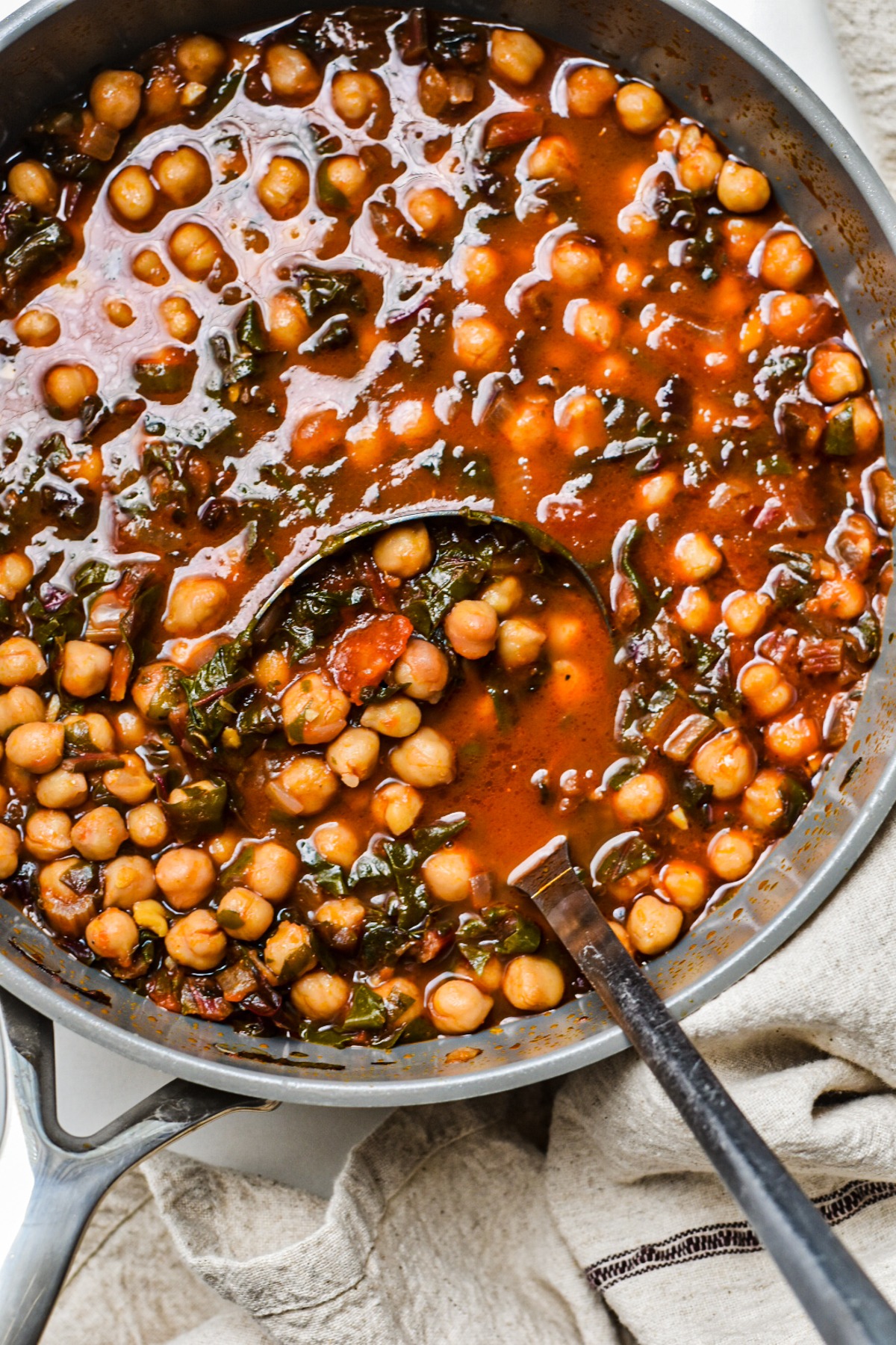 Overhead shot of a large pot of chickpea and Swiss chard soup with a ladle.