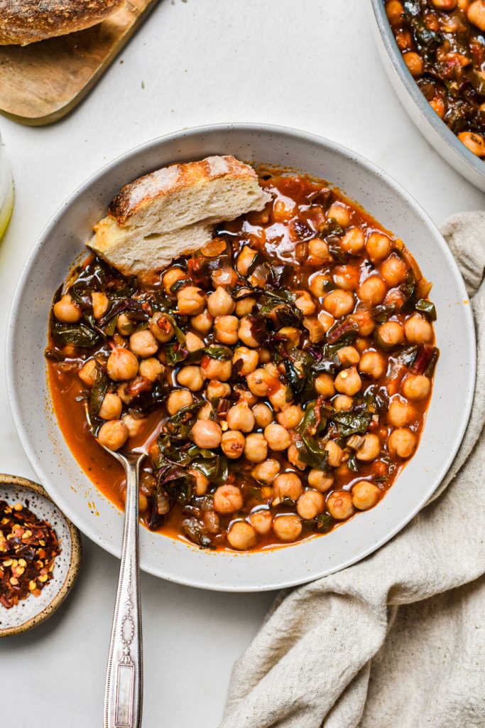 Overhead shot of a bowl of chickpea soup with Swiss chard with bread on the side.