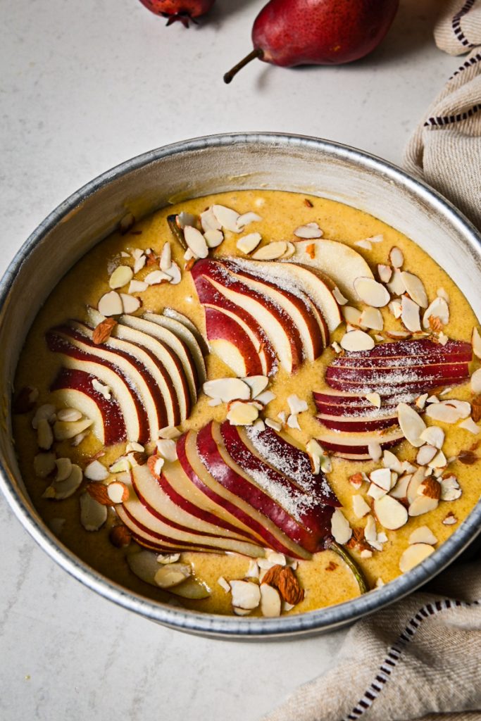 Cake batter in a cake pan with sliced pears and almonds on top.