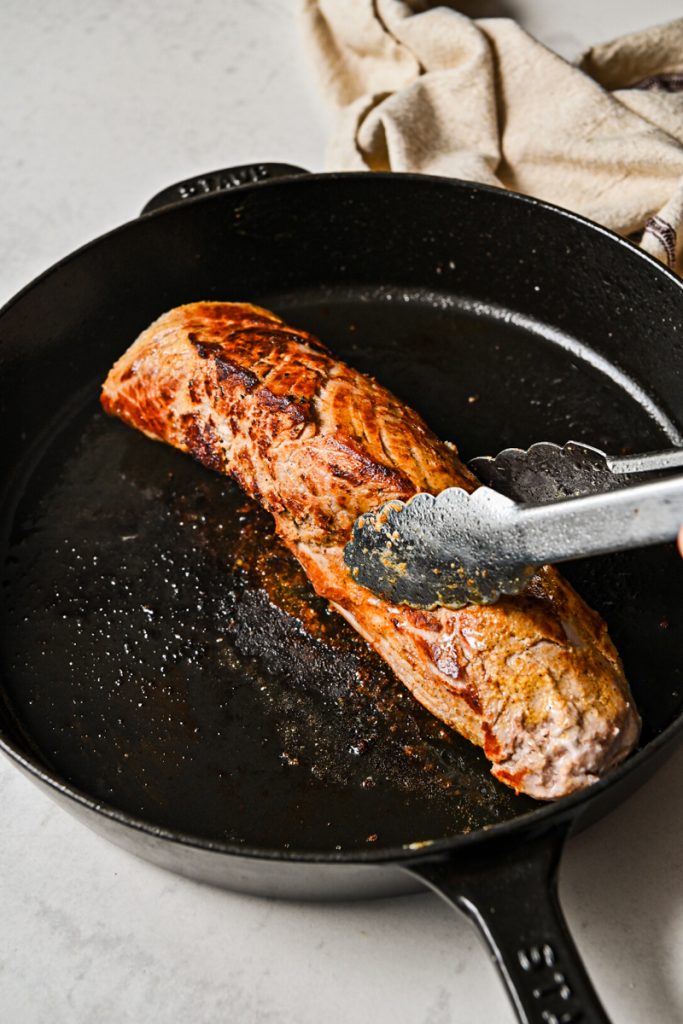 Pork loin searing in a cast iron skillet.