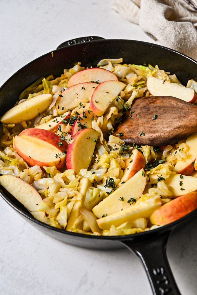 Apples and thyme added to the cabbage and onions in a skillet.