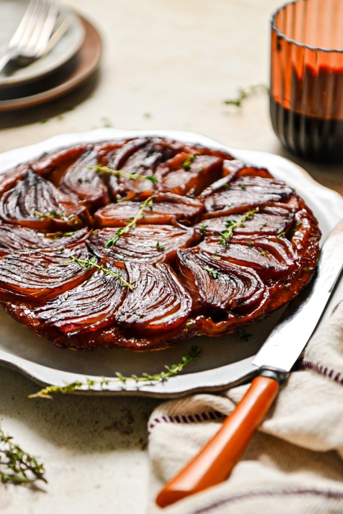 Red wine onion tart served on a platter with fresh thyme garnishing on top.