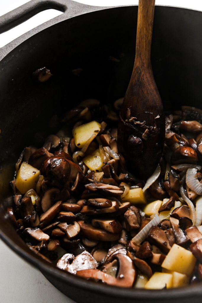 Potatoes, onion and mushrooms cooking in a large pot.