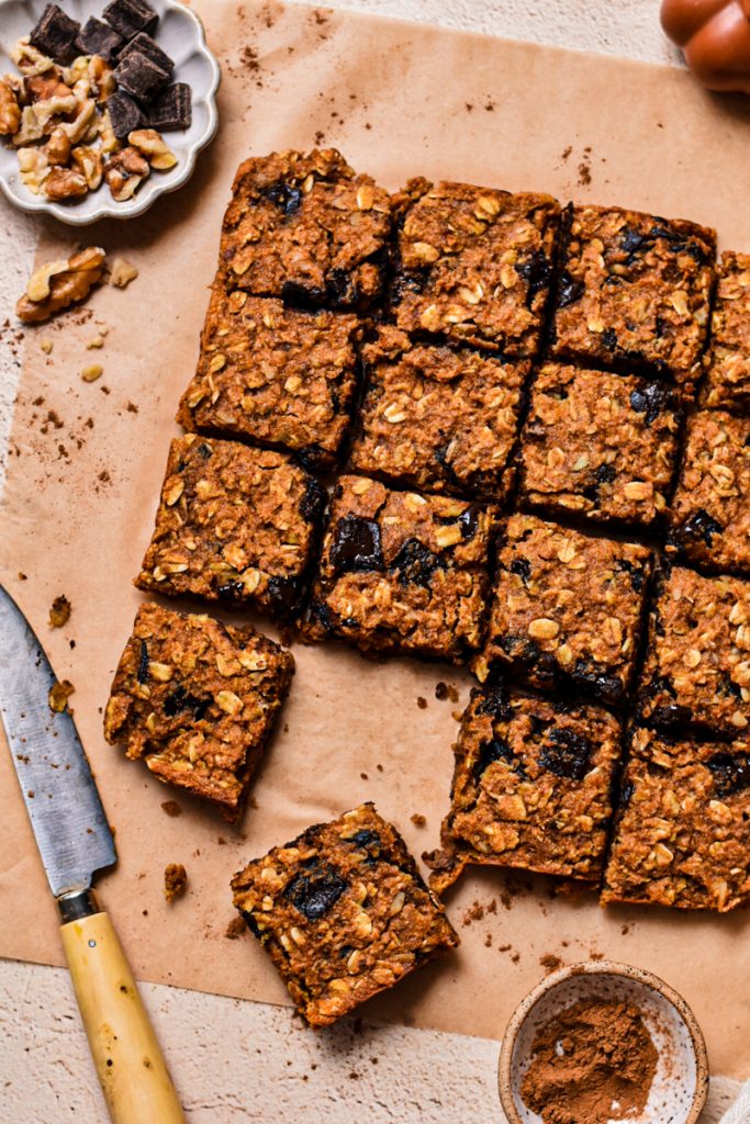 Close up of pumpkin chocolate baked oats sliced into squares on a parchment paper.