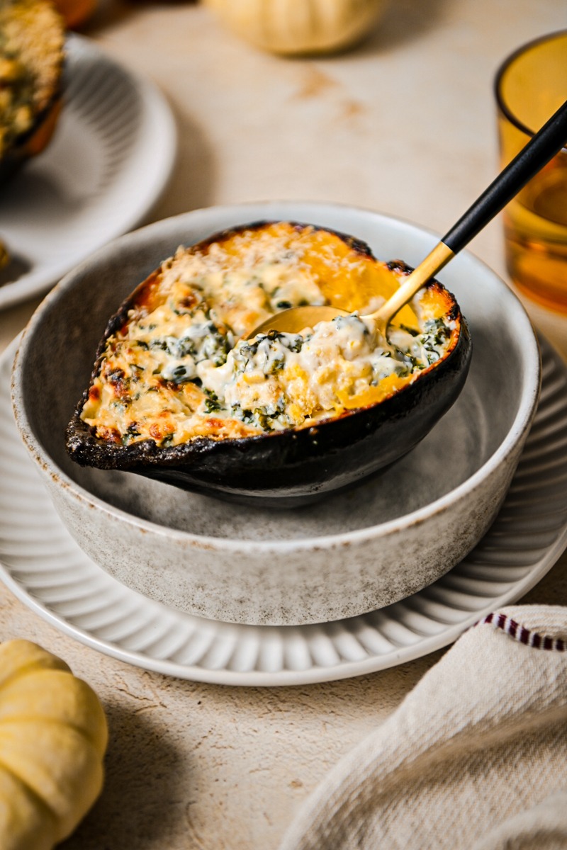 Side view of creamed kale and goat cheese stuffed acorn squash with a spoon taking a bite.