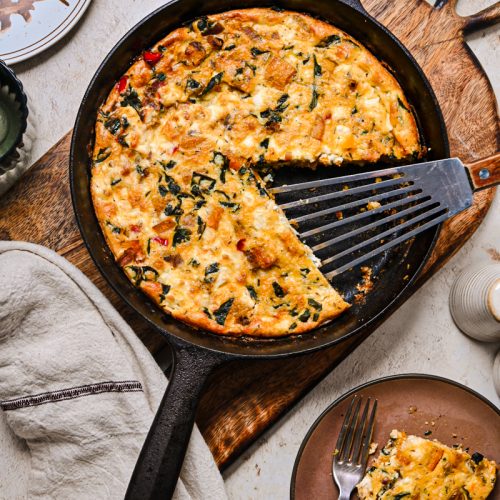 Overhead shot of butternut squash feta skillet quiche in a cast iron skillet with a piece missing.