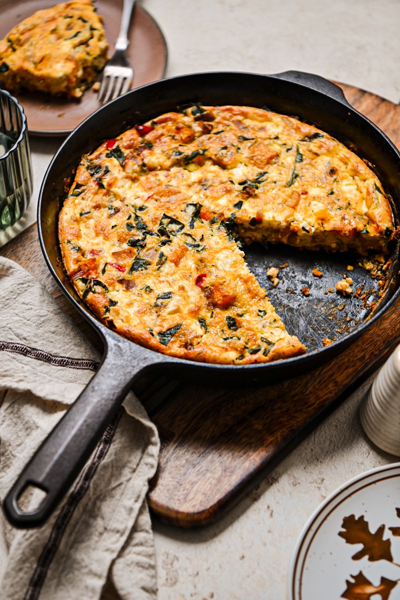 Butternut squash quiche in a cast iron skillet with one slice missing.