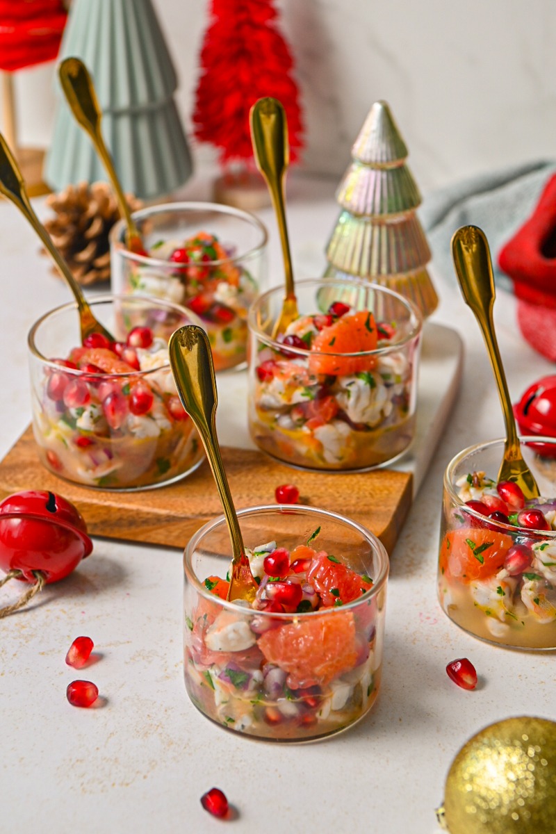 Citrus pomegranate shrimp ceviche served in five small glasses with gold spoons.