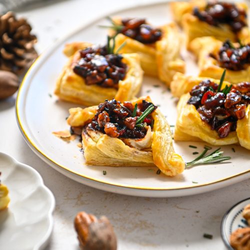 Side view of pecan brie bourbon bacon bites served on a platter with rosemary on top.