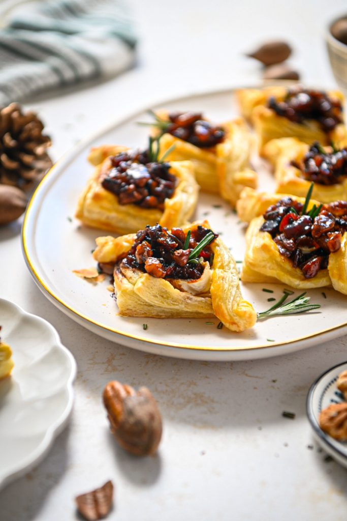 Side view of pecan brie bourbon bacon bites served on a platter with rosemary on top.