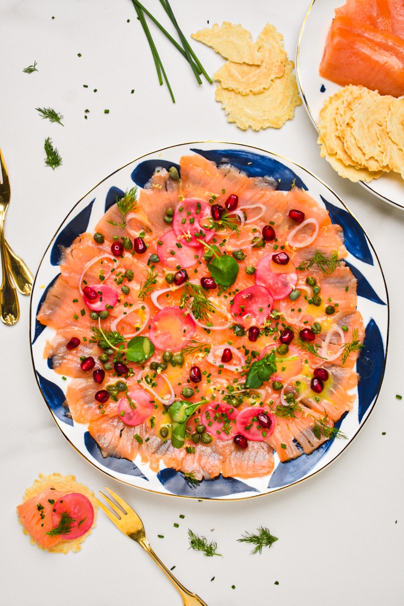 Smoked salmon carpaccio served on a plate with toppings and dressing.