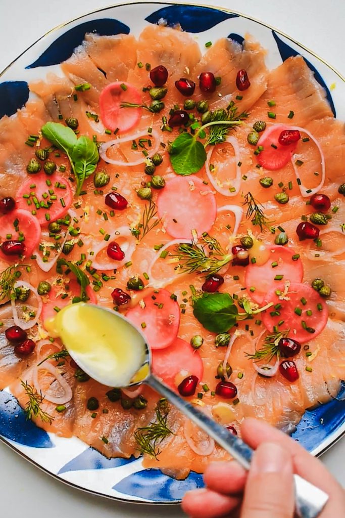 Using a spoon to drizzle dressing on top of the smoked salmon carpaccio.