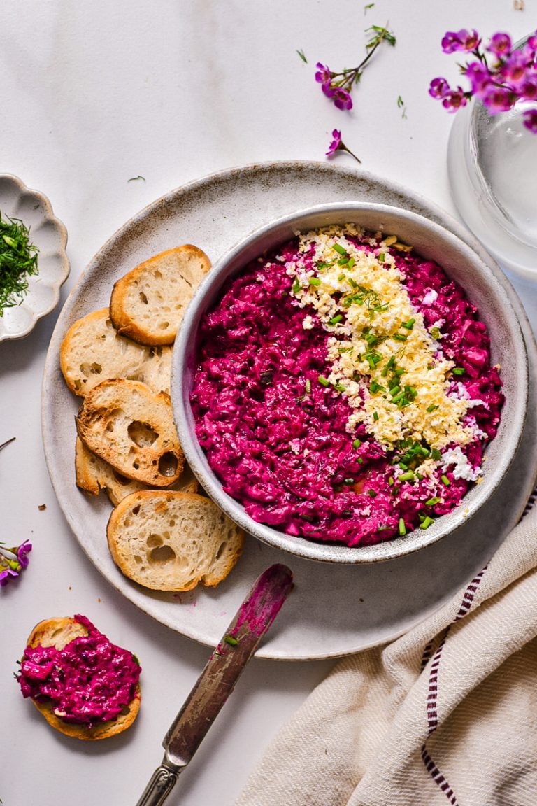 Bowl of beetroot and tuna dip served on a plate with crostini on the side.
