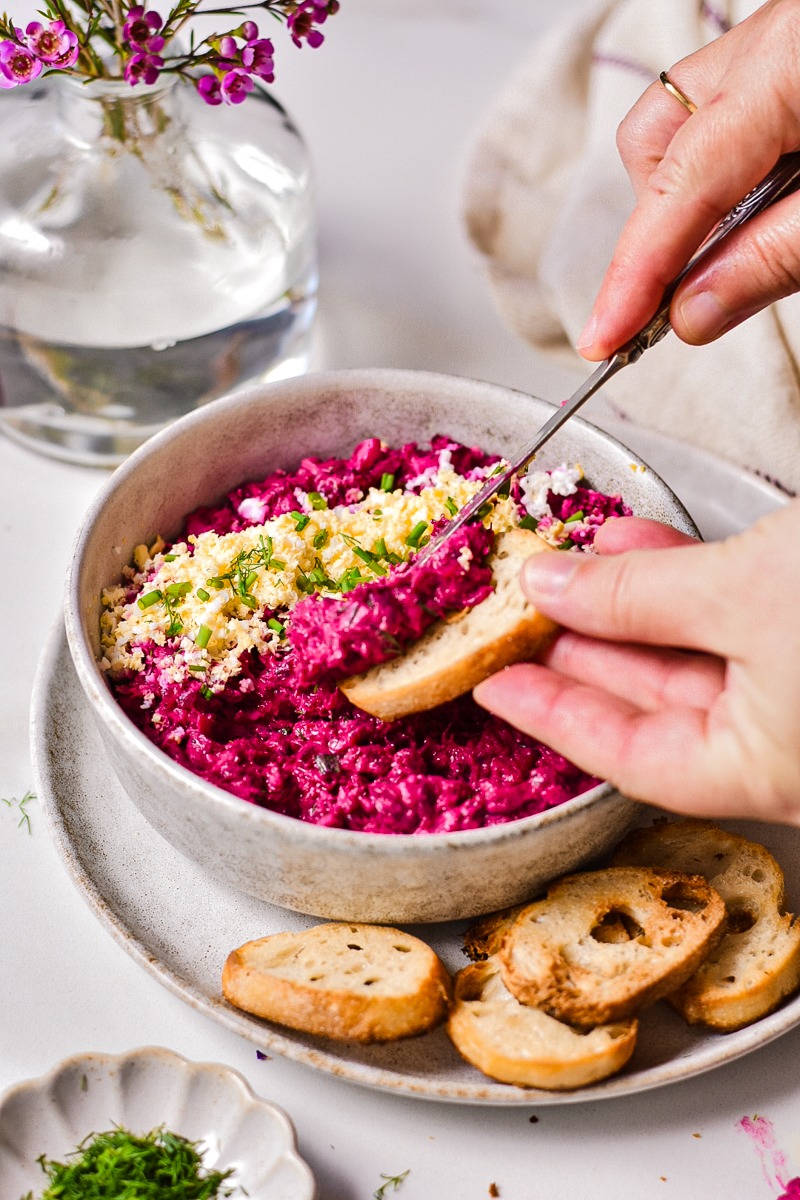 Hand spreading beetroot and tuna dip onto a crostini.