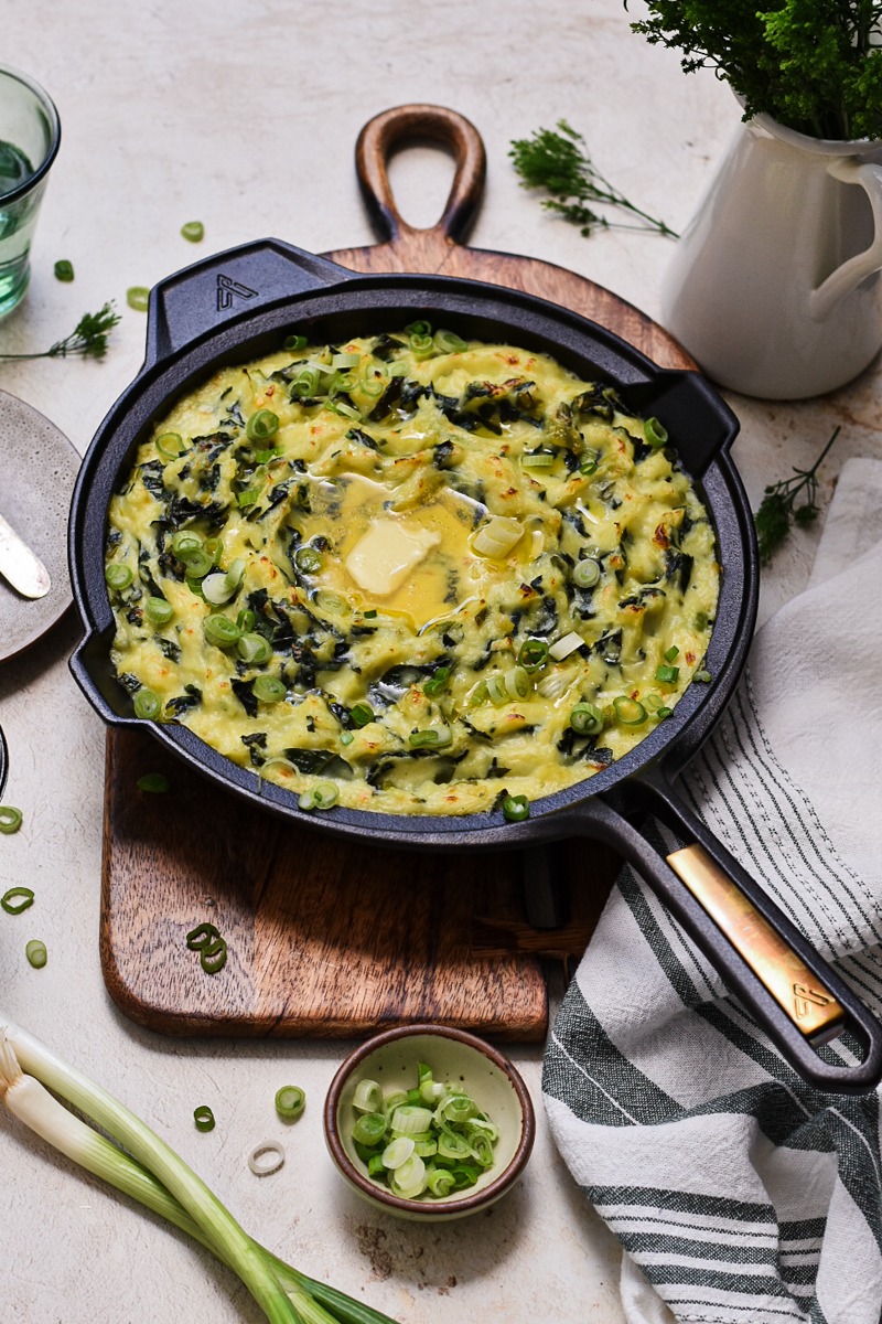 Skillet on a wooden board with Irish colcannon and melted butter on top.