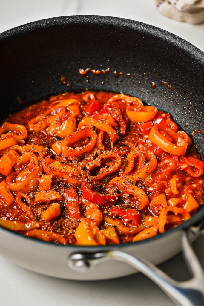 Spices added to sweet peppers and tomato paste in a skillet.