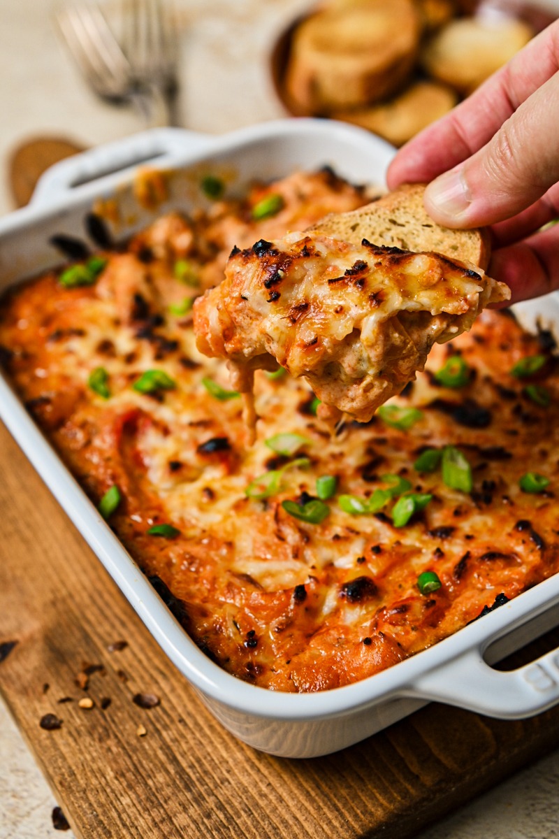 Hand dipping a crostini into the baked ricotta dip.