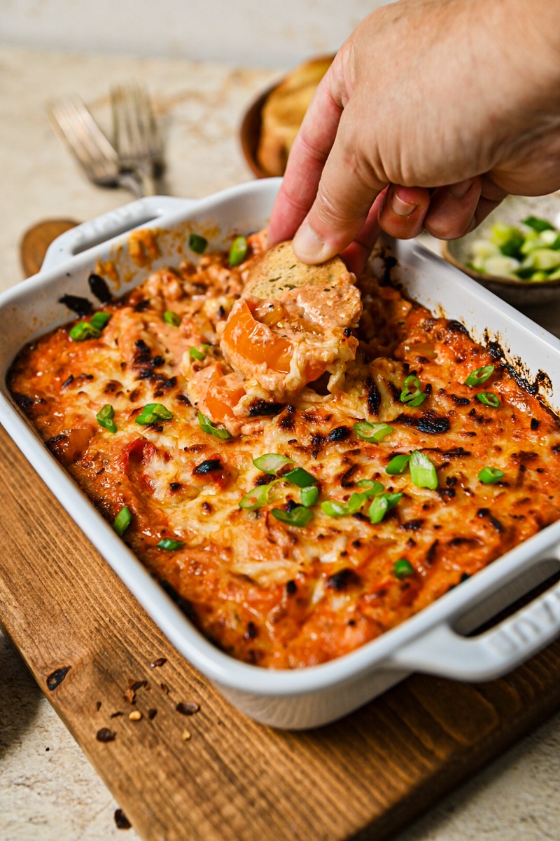 Hand dipping a crostini into the ricotta dip with sweet peppers.